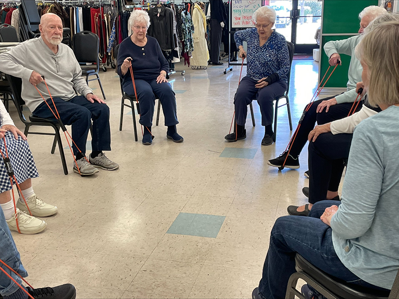 Seniors in a circle sitting in chairs doing exercises with tubes.
